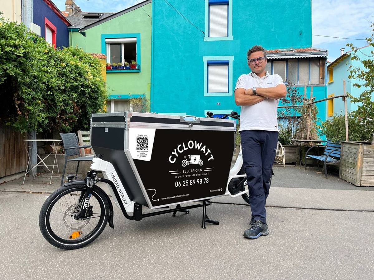 L'électricien de Cyclowatt devant son vélo cargo floqué, dans une rue aux façades colorées